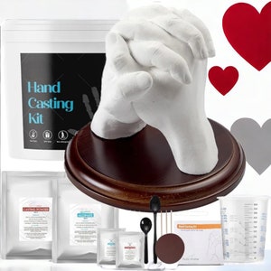 May include: A hand casting kit with all the necessary materials to create a plaster cast of two hands holding each other. The kit includes casting powder, alginate, a wooden base, two spoons, two stirring sticks, a measuring cup, and instructions. The kit is packaged in a white box with the words "Hand Casting Kit" printed on it.
