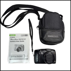May include: A black Canon PowerShot SX110 IS digital camera with a 10x optical zoom lens, a black Mainstays camera carrying case with a shoulder strap, and a printed Canon PowerShot SX110 IS Camera User Guide booklet with Getting Started text.