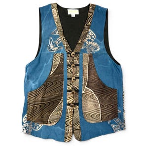 May include: A sleeveless vest featuring a blue base with dark brown and tan wavy, marbled patterns. The garment has a black interior lining, a V-neckline, and five circular buttons with black cord loops down the center front. Two large pockets are visible.