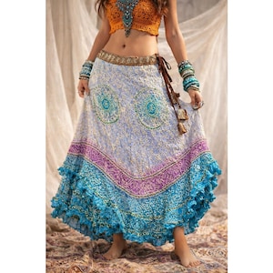 May include: A long, flowing skirt with a light blue background and intricate patterns. The skirt features a turquoise ruffled hem and a purple band. A brown tie belt and a matching orange crochet top complete the bohemian look.