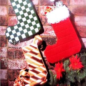 May include: Three Christmas stockings with different designs. The first stocking is green and white checked, the second is red with white trim, and the third is brown and white striped. The stockings are hanging on a brick wall with red poinsettia flowers.