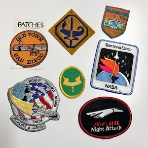 以下が含まれることがあります： 8つの刺繍パッチのセット。パッチには、スペースシャトル、建物、トーチ、ロケット、飛行機など、さまざまなデザインが施されています。パッチはすべて異なる色とサイズです。