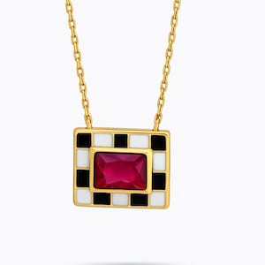 May include: A gold-toned necklace with a square pendant featuring a checkerboard pattern of black and white squares. The center of the pendant holds a rectangular, ruby-red gemstone. The necklace chain is also gold-toned.