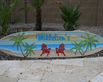 May include: A painted wooden surfboard with a beach scene, two red chairs, palm trees, and the text "Mikkelson's".