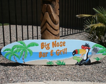 May include: A surfboard sign painted with a blue ocean scene, palm trees, and a toucan drinking a cocktail. The sign reads "Big Nose Bar & Grill".
