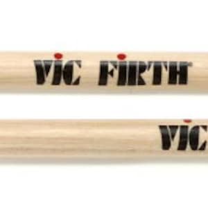 Puede incluir: Dos baquetas de bater&iacute;a de madera clara, con la inscripci&oacute;n "VIC FIRTH" y "WORLD CLASSIC CONQUISTADOR". Las baquetas son de color marr&oacute;n claro y tienen una firma.