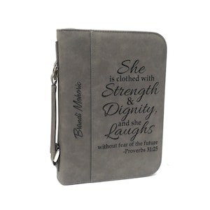 May include: Gray faux leather Bible cover with a personalized name and the inscription "She is clothed with Strength & Dignity, and she Laughs without fear of the future -Proverbs 31:25".