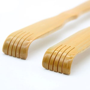 May include: Two wooden back scratchers with curved handles and five rows of teeth. The scratchers are made of natural bamboo and have a light brown color.