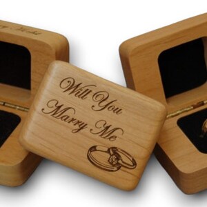 May include: Three wooden ring boxes. One box is engraved with "Will You Marry Me" and two rings. Another box is engraved with "Rangeview High School" and a red ring. The third box is empty.