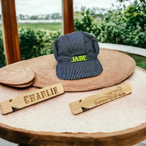 May include: Two wooden name tags with the names "Charlie" and "Jade" engraved on them. The name tag with "Jade" is next to a blue and white striped engineer's cap with the name "Jade" embroidered on it.