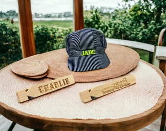 May include: Two wooden name tags with the names "Charlie" and "Jade" engraved on them. The name tag with "Jade" is next to a blue and white striped engineer's cap with the name "Jade" embroidered on it.