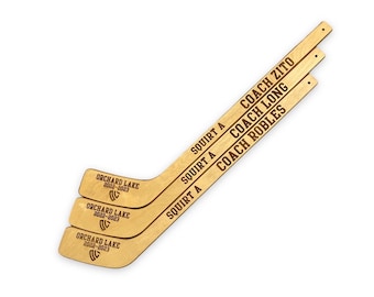 May include: Three wooden hockey sticks with the text "SQUIRT A" and the names of coaches: "COACH ZITO", "COACH LONG", and "COACH ROBLES". The sticks also have the text "ORCHARD LAKE 2022-2023" printed on them.