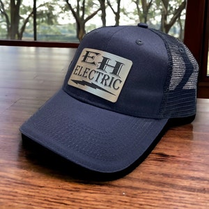 May include: A navy blue trucker hat with a silver patch that says "E.H. Electric" with a lightning bolt graphic.
