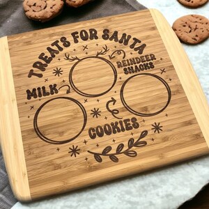 May include: A brown bamboo cutting board with the text "Treats for Santa" and spaces for milk and cookies. The board has a decorative reindeer design and the words "Reindeer Snacks".