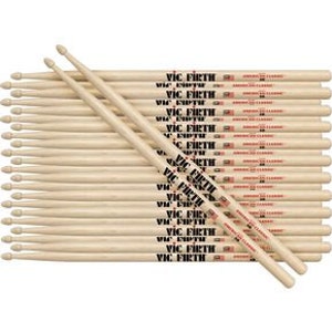Puede incluir: Un conjunto de baquetas Vic Firth American Classic 5A. Las baquetas son de madera clara y presentan el logotipo de Vic Firth y un dise&ntilde;o de bandera estadounidense. Las baquetas est&aacute;n dispuestas en un mont&oacute;n ordenado.