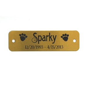May include: Gold metal pet memorial tag with black paw prints and the text "Sparky 12/20/1993 - 4/15/2013".