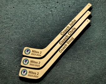 May include: Three wooden hockey sticks with the text "Mites 2 2023-2024" and the names "Coach John", "Coach Chris", and "Coach Doug" engraved on them.