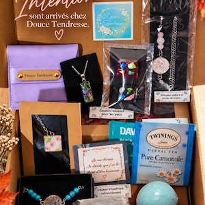 Può includere: Una scatola regalo contenente una pochette viola, una collana con ciondolo rettangolare, un diffusore per auto, una collana con ciondolo floreale quadrato, un braccialetto con perline blu e ciondolo ad albero, una bustina di tè Twinings, una bomba da bagno e una pietra pomice.