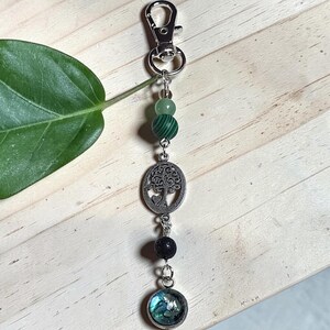 Può includere: Un portachiavi in metallo color argento con chiusura a moschettone, una perlina verde chiaro, una perlina in malachite verde a righe, un ciondolo circolare con albero e cuore, una perlina in pietra lavica nera e un ciondolo rotondo in abalone.