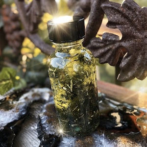 May include: A small glass bottle filled with a clear liquid and green herbs. The bottle has a black screw-on cap. The bottle is sitting on a wooden surface.