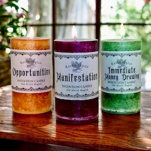 May include: Three lit intention candles with labels that read "Opportunities", "Manifestation", and "Immediate Money Drawing". The candles are orange, purple, and green, respectively, and are on a wooden surface.
