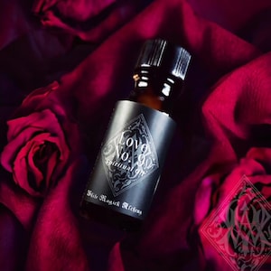 May include: A small, dark brown glass bottle with a black label that reads "Love No. 90 Spiritual Oil" and "White Magick Alchemy". The bottle is sitting on a red velvet fabric.