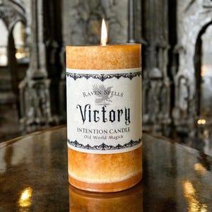 May include: A brown candle with a white label that reads "Raven Spells Victory Intention Candle Old World Magick".