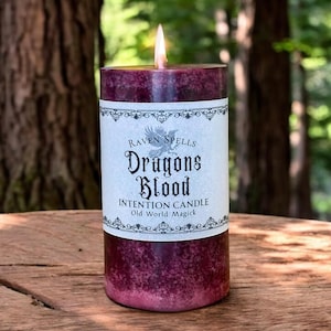 May include: A dark red candle with a white label that reads "Raven Spells Dragons Blood Intention Candle Old World Magick".