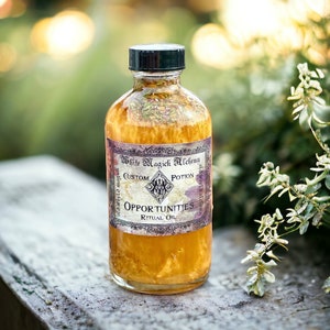 May include: A glass bottle with a gold liquid and a label that reads "White Magick Alchemy Custom Potion Opportunities Ritual Oil". The bottle is sitting on a wooden surface with green foliage in the background.