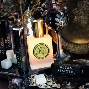May include: Three bottles of Gothic Absinthe essential oil, one in a clear glass bottle with a gold cap and two in roller bottles. The bottles are on a dark surface with sugar cubes and a silver sugar tongs.