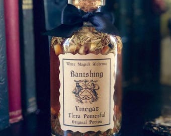 May include: A glass bottle with a cork stopper and a black ribbon tied around the neck. The bottle is filled with a brown liquid and herbs. The label reads "White Magick Alchemy Banishing Spells for Magic Vinegar Ultra Powerful Original Potion".