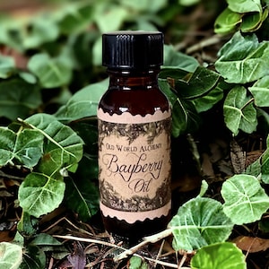 May include: A small brown glass bottle with a black cap, sitting on a bed of green leaves. The bottle has a label that reads "Old World Alchemy Bayberry Oil".