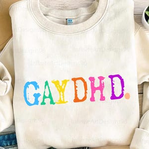May include: A cream colored sweatshirt with the text "GAY DHD" printed in rainbow colors.