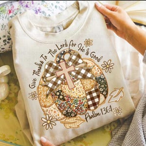 May include: A cream-coloured sweatshirt with a pumpkin design, a cross, and a bow. The pumpkin is made of patchwork fabric with floral and plaid patterns. Text includes "Give Thanks To The Lord for He is Good" and "Psalm 136:1".