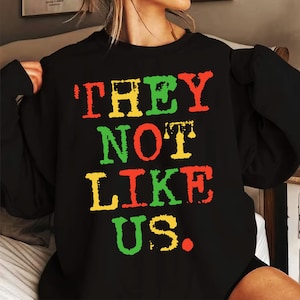 May include: Black sweatshirt with the text "THEY NOT LIKE US." in red, yellow and green letters.