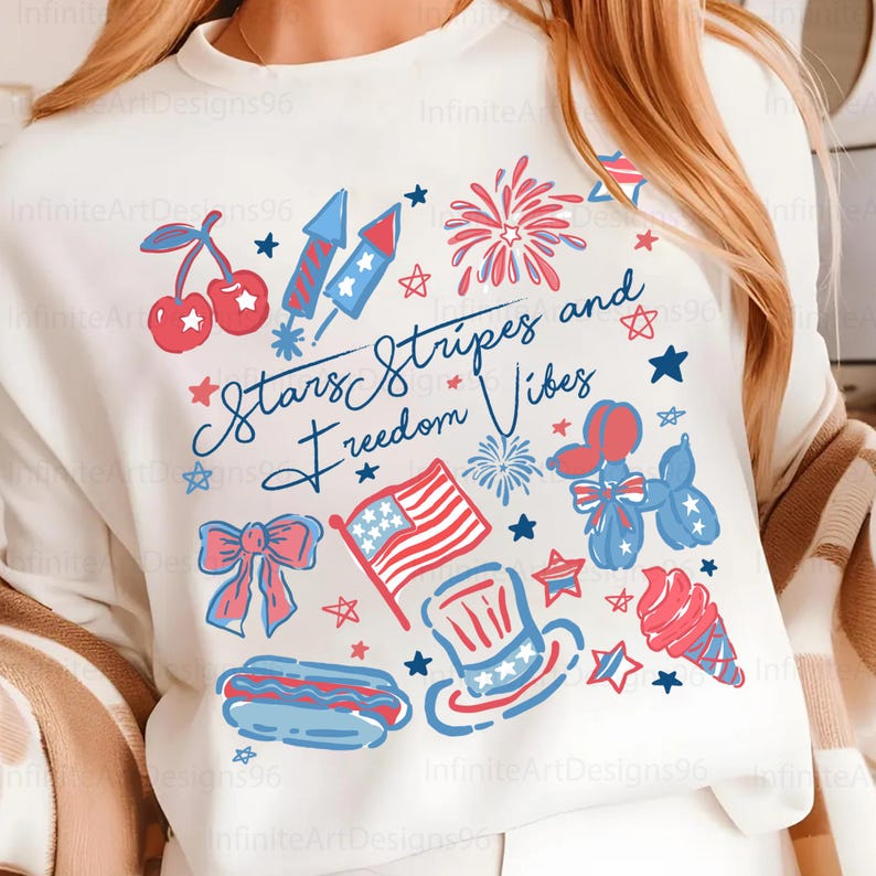 May include: White sweatshirt with a patriotic design featuring cherries, fireworks, an American flag, and a hot dog. The text "Stars Stripes and Freedom Vibes" is written in blue script. Red, white, and blue colors.