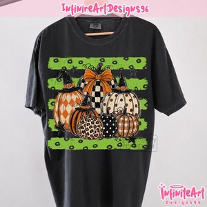 Può includere: Una t-shirt nera a maniche corte con una stampa grafica di diverse zucche con vari motivi, tra cui stampa leopardata, pois e quadri. Alcune zucche indossano cappelli da strega neri e una presenta un fiocco arancione su sfondo a righe.