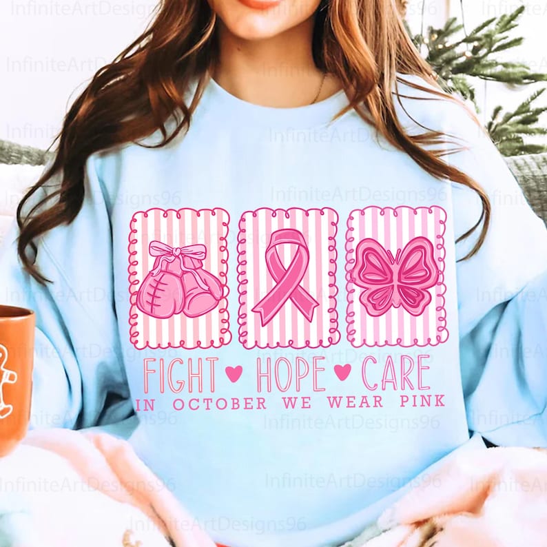 May include: Light blue sweatshirt with a pink design featuring boxing gloves, a ribbon, and a butterfly. The text reads "FIGHT HOPE CARE" and "IN OCTOBER WE WEAR PINK". A design for breast cancer awareness.
