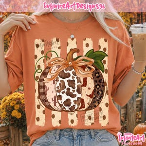 Puede incluir: Una camiseta naranja con un gráfico central de una calabaza con un lazo. La calabaza tiene secciones con estampado de vaca, leopardo y cuadros. Detrás de la calabaza hay rayas verticales con lunares y el texto InfiniteArtDesigns96.