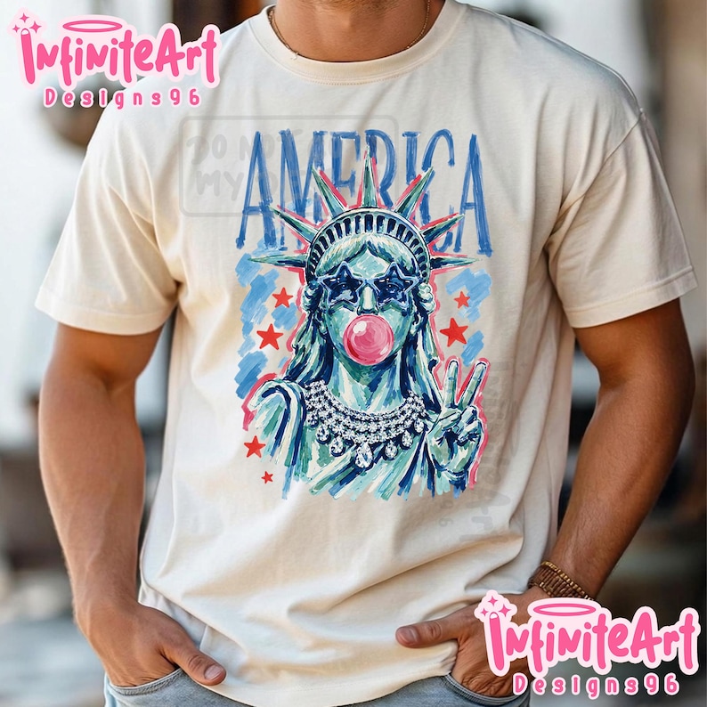 May include: A cream-coloured t-shirt featuring a graphic of the Statue of Liberty wearing star-shaped sunglasses and blowing a pink bubblegum bubble. The word AMERICA is printed in blue above the figure, accompanied by red stars and blue brushstrokes.