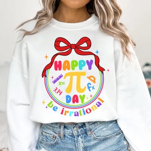 May include: White sweatshirt with a rainbow graphic that says "Happy Pi Day be irrational". The graphic includes a red bow, a ruler, a protractor, and the number pi.