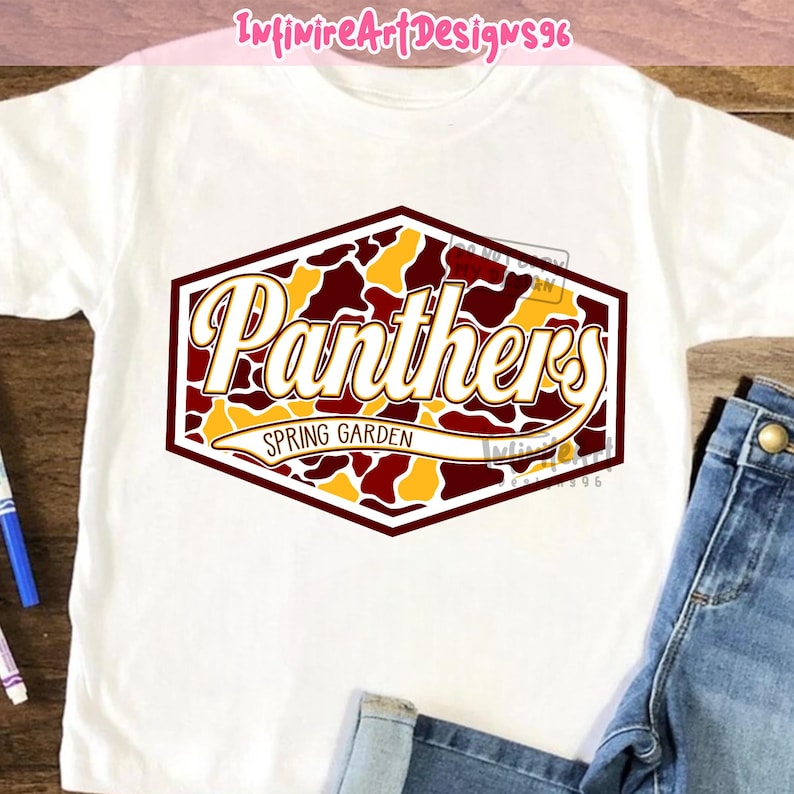 Op de afbeelding: Een wit t-shirt met een zeshoekige afbeelding in een bordeauxrood, goud en wit camouflagepatroon. De tekst "Panthers" is geschreven in een groot, vet, wit scriptlettertype, met "SPRING GARDEN" in een kleiner lettertype op een witte banner.