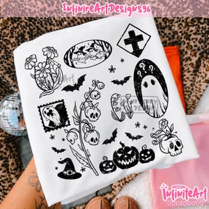 Puede incluir: Una camiseta blanca con un estampado gráfico negro de varias ilustraciones con temática de Halloween, que incluyen fantasmas, calaveras, calabazas, murciélagos, flores, un sombrero de bruja y una cruz. El diseño tiene un aspecto desgastado.