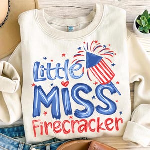 May include: Cream-colored sweatshirt with the text "Little Miss Firecracker" in blue and red. A graphic of a firework is also featured. The design is perfect for celebrating Independence Day or other patriotic events.