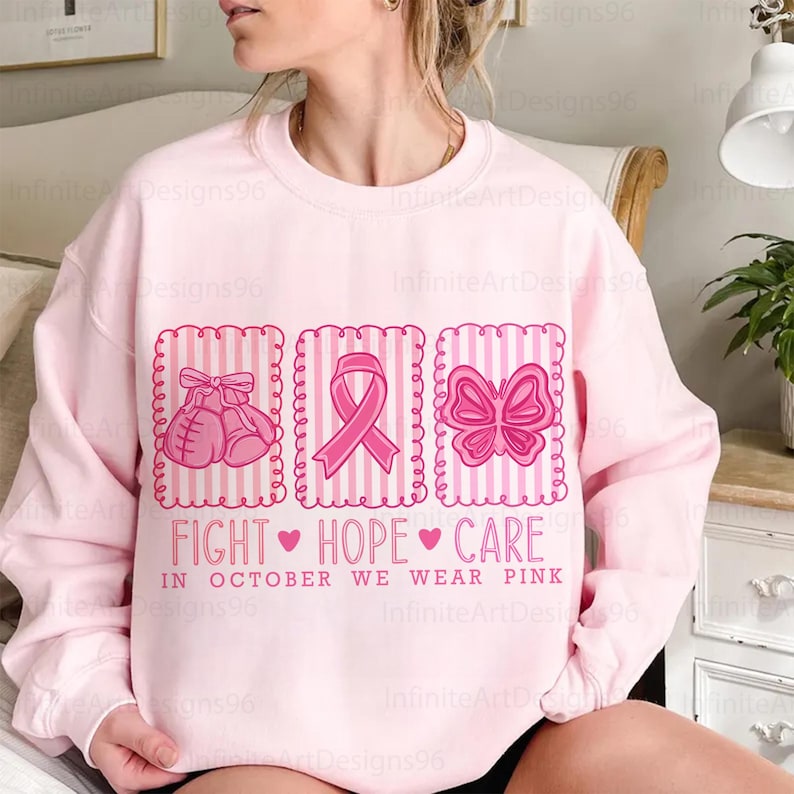 May include: A light pink sweatshirt with a graphic design featuring pink boxing gloves, a ribbon, and a butterfly. The text reads "FIGHT HOPE CARE" and "IN OCTOBER WE WEAR PINK".
