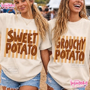 May include: Two cream-colored t-shirts featuring brown vertical stripes and brown text. One shirt displays the words SWEET POTATO, while the other displays the words GROUCHY POTATO. Both shirts have short sleeves and a crew neckline, with a casual fit.