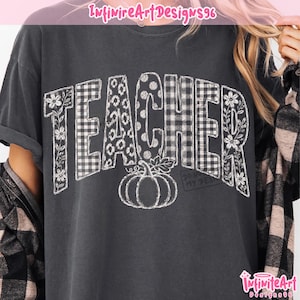 May include: A charcoal grey short-sleeved t-shirt featuring the word TEACHER in large white block letters. Each letter has a unique pattern including floral, plaid, and polka dot designs. A white line-art pumpkin sits below the word.