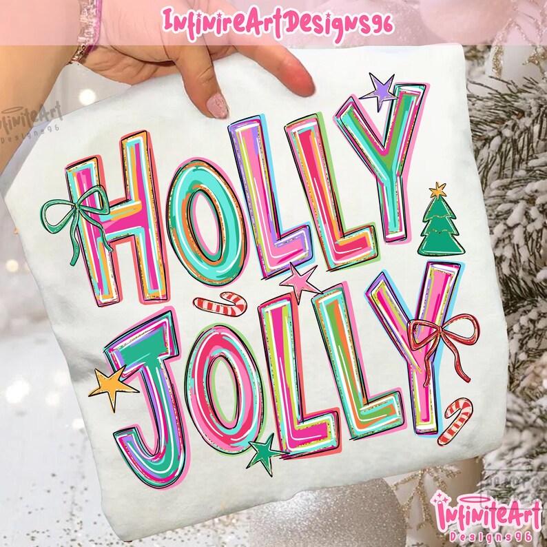 May include: A white t-shirt featuring the text HOLLY JOLLY in large, multi-colored block letters with pink, teal, and orange stripes. The design includes a green Christmas tree, two candy canes, three stars, and two bows in teal and red.