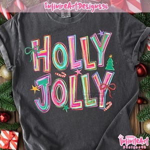 May include: A charcoal gray short-sleeve t-shirt featuring the text HOLLY JOLLY in large, colorful, multi-layered block letters. The design includes small graphic elements such as a green bow, a green Christmas tree, stars, and candy canes.