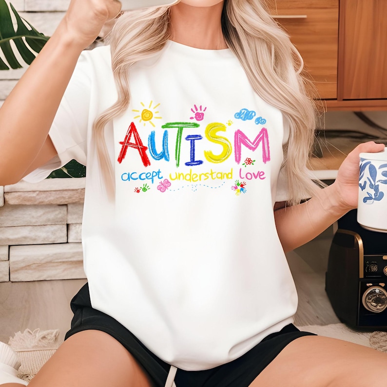 Puede incluir: Camiseta blanca con un gr&aacute;fico colorido que dice "AUTISMO aceptar comprender amar".